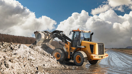 A yellow loader is moving large piles of dirt and rubble on a construction site. The weather is...