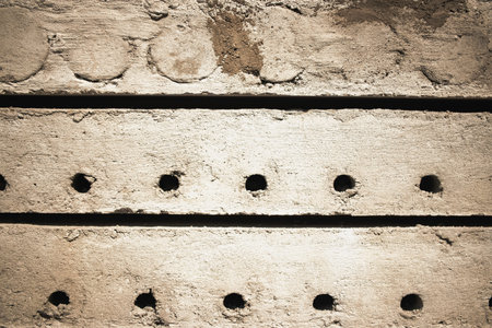 Close-up view of a textured concrete wall featuring evenly spaced holes. The surface shows signs of recent work, typical of a construction site.の写真素材