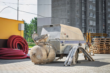 Construction equipment is parked at a site near a residential building, alongside hoses and wooden pallets under a clear blue sky.の写真素材