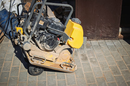 Heavy construction equipment is parked on a brick surface at a building site, surrounded by various materials and tools, under clear skies.の写真素材