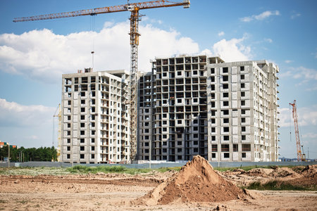 Workers are busy at a construction site where two large residential buildings are being built, surrounded by machinery and earth piles.の写真素材