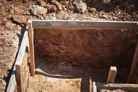 A trench is seen at a construction site with wooden supports. The dry earth reveals rich soil layers under a clear blue sky in the afternoon light.の写真素材