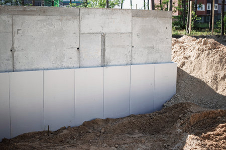 Workers are engaged in constructing a foundation at a construction site, featuring a concrete wall and prepared soil for structural support.の写真素材