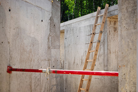 Bright daylight illuminates a construction site featuring concrete walls and a wooden ladder,...