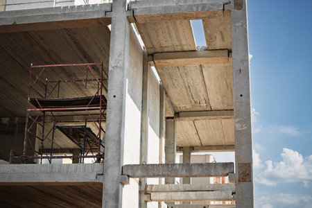 Workers oversee construction progress on a multi-story building with exposed concrete and scaffolding during a sunny afternoon.の写真素材