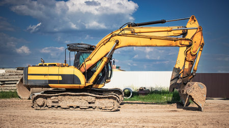 A yellow excavator is located on a construction site, showcasing its large tracks and digging arm in bright sunlight against a blue sky.の写真素材