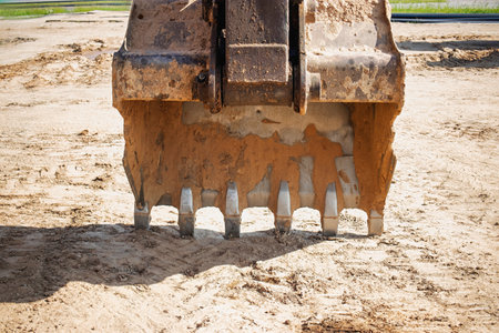 Heavy machinery is actively engaged in excavation, with the bucket gripping the earth and dirt getting displaced under the bright sunlight at a construction site.の写真素材