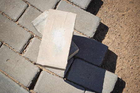 A construction worker skillfully places pavers on a patio surface under clear skies. Sunlight casts shadows, highlighting the precision of the work.の写真素材