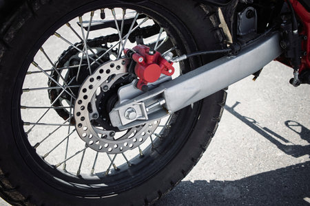 The intricate details of a motorcycle's rear wheel, featuring a disc brake and spokes, are highlighted under bright sunlight during outdoor exploration.の写真素材