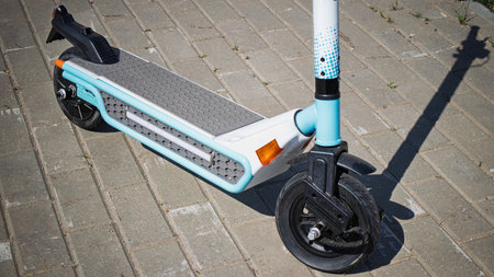 An electric scooter stands on a brick pathway in a lively urban environment, showing its sleek design under the bright sun.の写真素材