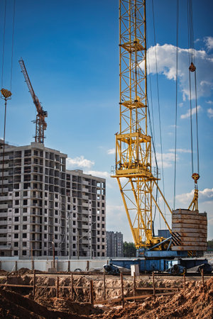 A yellow crane operates at a construction site, lifting building materials as workers continue work on a rising apartment complex under a blue sky.の写真素材