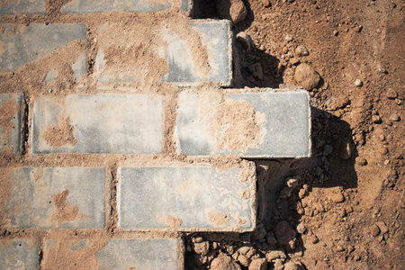 A newly laid brick pathway sits partially completed with dirt and gravel surrounding the edges, illuminated by bright sunlight in an outdoor setting.の写真素材