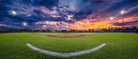 Lush grass glows under stadium lights as a vibrant sunset paints the sky, setting the stage for an exhilarating night of baseball action.の素材