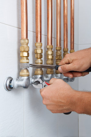 A skilled plumber is working on a water heating system, utilizing pliers on copper pipes within a stylish modern home setup. The focus is on craftsmanship and detail.の素材