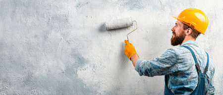 A dedicated man in a work uniform paints a wall with a roller, showcasing his craftsmanship and creativity in a bright and well-lit workspace.の素材