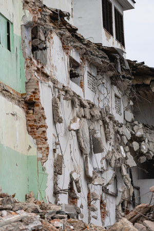 Construction workers are actively dismantling a building, exposing its internal structures and leaving piles of debris on the ground at the site.の写真素材