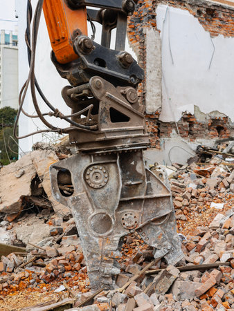 A powerful excavator is actively dismantling a building, clearing debris and rubble from the urban site. The demolition showcases heavy machinery in action.の写真素材