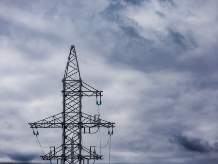 A towering structure for high voltage electricity stands tall under a dramatic sky filled with...