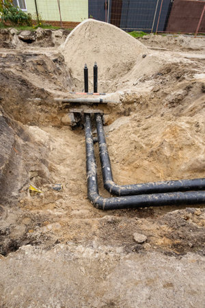 Workers are installing black pipes in a dug-up section of ground, showing the process of preparing for underground utilities in a construction area.の写真素材
