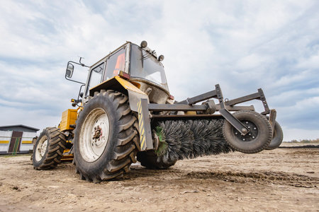 A tractor uses a brush attachment to clear mud and debris from a farm field, showcasing the machinery's function in agricultural maintenance.の写真素材