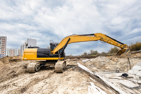 Excavator moves dirt at a construction site with apartment buildings in the background under...