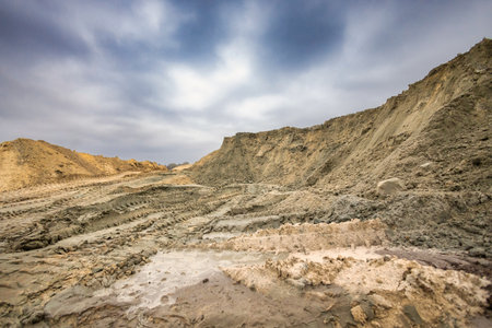 Heavy machinery has moved large amounts of earth, creating mounds and deep tracks at a construction site under a cloudy sky in the afternoon.の写真素材