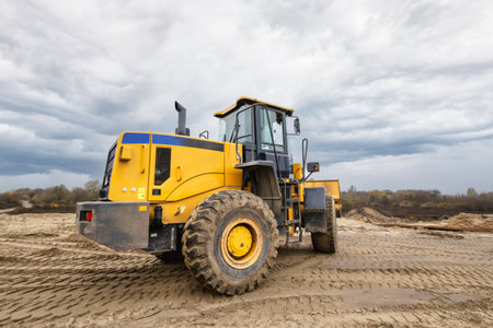A large yellow bulldozer sits on a construction site, surrounded by sand and dirt, under an overcast...