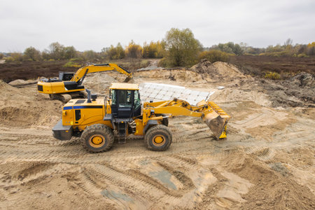 Heavy machinery is actively working at a construction site in autumn. A loader and an excavator are...