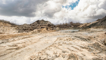 A vast area shows dry, cracked earth and dirt mounds. The sky is partly cloudy, creating a stark contrast with the land in the foreground.の写真素材