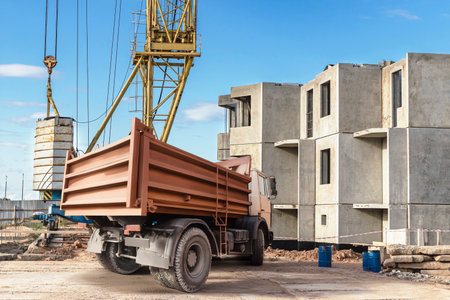 Heavy machinery works diligently at a construction site, as a truck unloads materials while a crane lifts heavy equipment into position under a clear blue sky.の写真素材