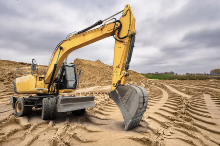 A yellow excavator maneuvers through a construction site, skillfully reshaping the sandy terrain as...