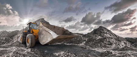 Large earth-moving equipment works tirelessly among towering piles of soil as the sun sets, casting...
