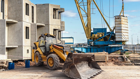 Excavators and cranes work together on a construction site, shaping new buildings. Workers...