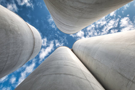 Factory chimneys stand tall against a clear blue sky, showcasing industrial strength and the bustling activity from below on a sunny afternoon.の素材