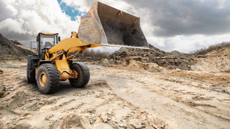 A loader moves dirt and debris at a construction site while clouds hang overhead. The equipment is at work preparing the area for development.の写真素材