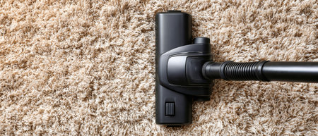 A vacuum cleaner works on a soft carpet, capturing dirt and dust. Sunlight fills the living room, creating a clean and fresh environment.の素材