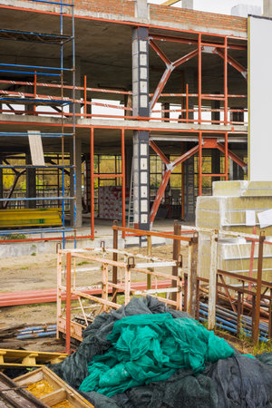 Workers are building a new structure with metal beams and scaffolding in an active construction area filled with various materials and tools.の写真素材
