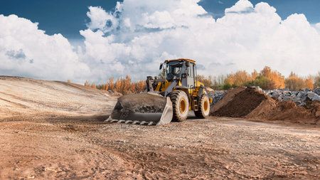 Loader is moving dirt on a construction site. The area is preparing for new structures with trees in...