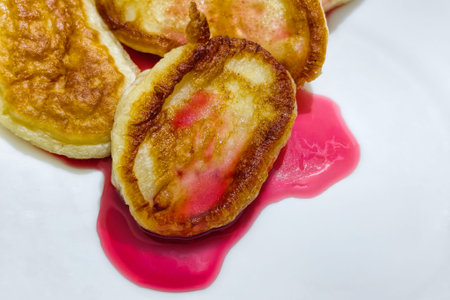 Pancakes sit on a white plate with red syrup pooled around them, ready to be eaten at breakfast or brunch with a focus on food presentation.の写真素材