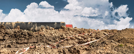 Construction workers are moving dirt at a work site. Clouds build in a blue sky above heavy...