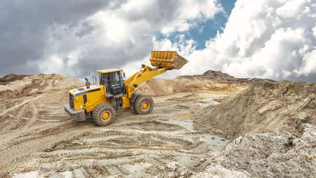 A large yellow loader moves earth and gravel at a construction site during the day, while clouds...