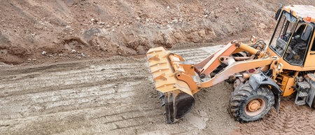 A powerful bulldozer or loader carefully clears and shapes sand at a construction site, preparing...