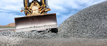 A large grader or bulldozer moves gravel at a construction site, skillfully preparing the area for...