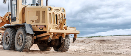 A large yellow grader grades the earth's surface for the construction of a future road or facility....