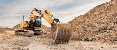 Heavy machinery moves soil and rocks at a construction site. The excavator digs into the ground...