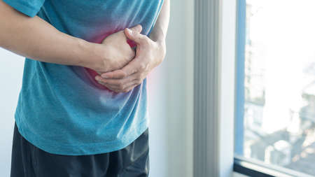 A young man had a stomach ache and touched on his stomach due to severe pain from stomach ailments in the hospital. Pain and viewing and health concept.の写真素材