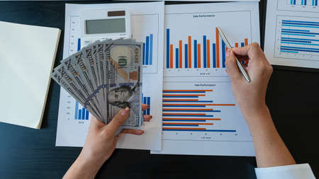A top view of a businessman holding a dollar and a pen pointing at the calculator graph on the table