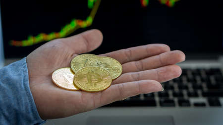 Bitcoins and virtual money concept Gold Bitcoins on the hands with a graph in the background, the...