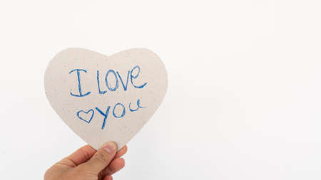 Heart-shaped paper representing love, hand written I love you on a white background.の写真素材