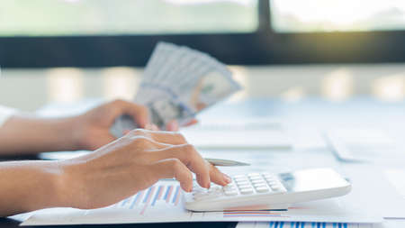 The young woman held a pen and pressed the calculator, the left hand held the dollar in a plan to calculate the financial in the office.の写真素材